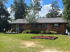 A wooden cabin with a metal roof, a porch, and a small deck. - Georgia Lake House Retreat (Donalsonville)