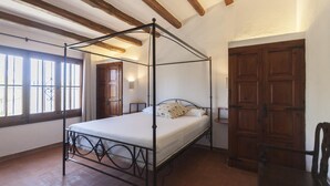 A room with a four-poster bed, wooden beams on the ceiling, a large wooden door, and a window with bars. - BIG HOUSE with BBQ and dining room outside (Tossa de Mar)