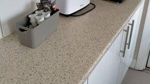 Una cocina con armarios blancos, un tostador, un microondas y un contenedor gris con objetos.