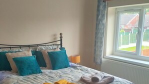 Un dormitorio con cama, almohadas, una lámpara y una ventana.