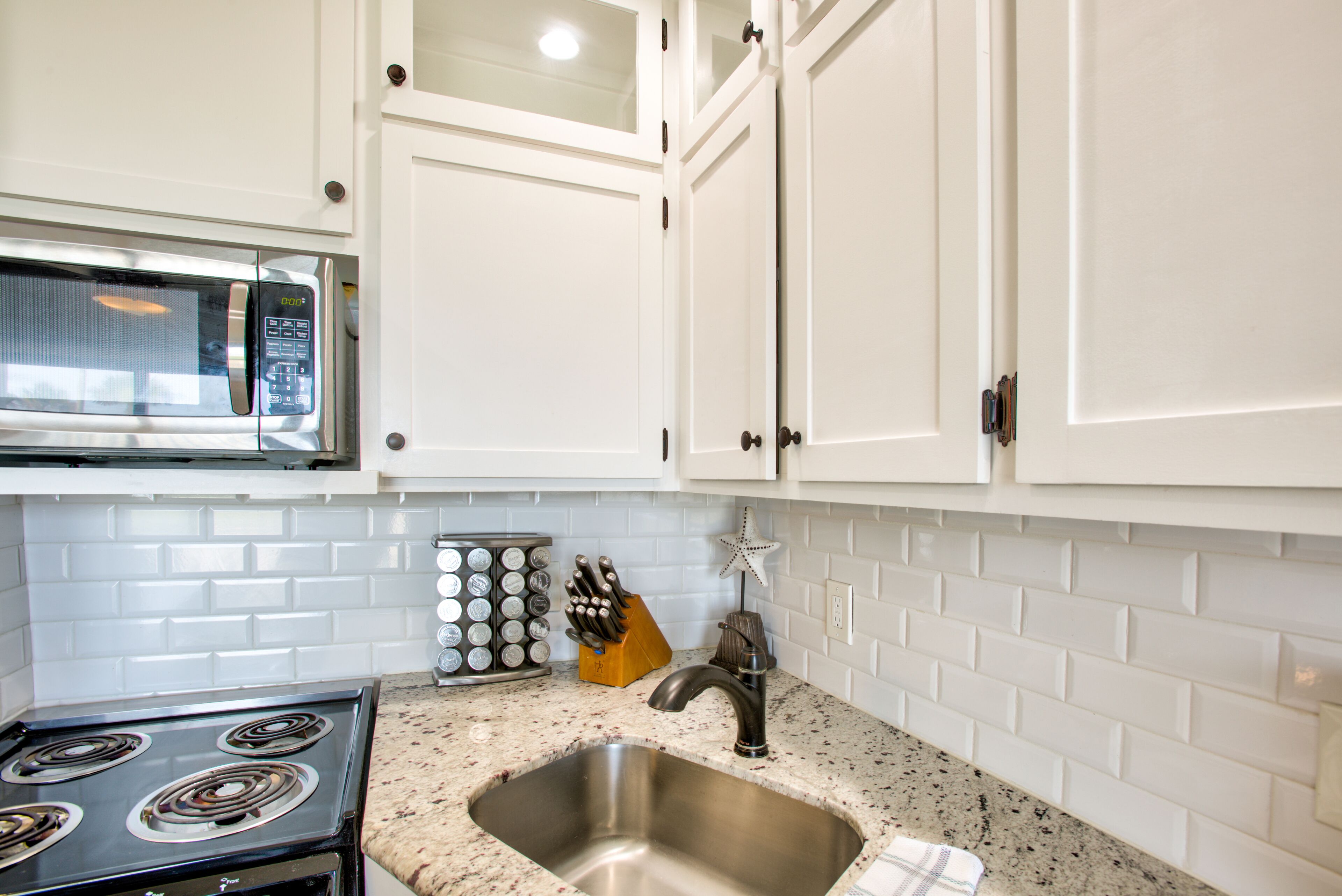 A kitchen with white cabinets, a stainless steel sink, a granite countertop, a stove, and a knife block.