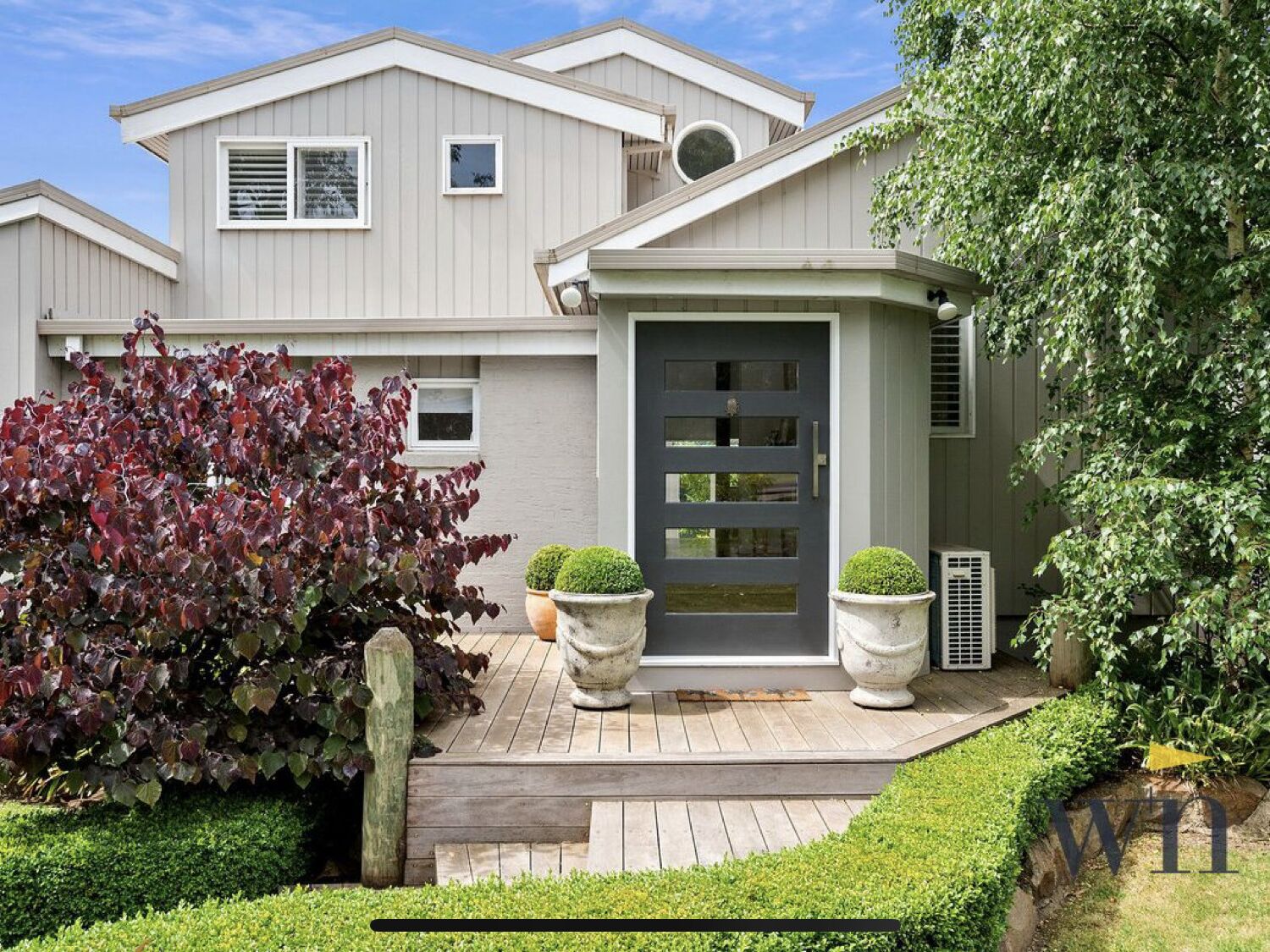 A two-story house with a grey exterior, a dark front door, and a small porch with two potted plants.