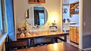 A bar area with a wooden sign, a round mirror, and a countertop with glasses and a candle holder.