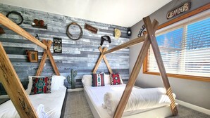 A room with two beds, a wooden ceiling structure, a wall with a 'CLEAN BEDS' sign, and a window with blinds.