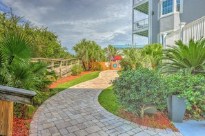 A pathway leading to a building with a balcony, surrounded by lush greenery and a wooden fence.