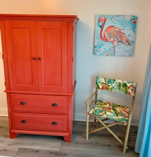 Un mueble rojo de madera con cajones y una silla con estampado de hojas tropicales.