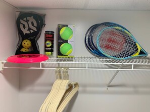 Una estantería con una raqueta de tenis, una lata de pelotas de tenis y una bolsa de pelotas de tenis.