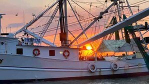 Ein großes Fischerboot liegt im Hafen vor einem Sonnenuntergang.