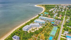 Luftaufnahme eines Küstenresorts mit Strandhäusern, einem großen Hotelkomplex und einem Tennisplatz.