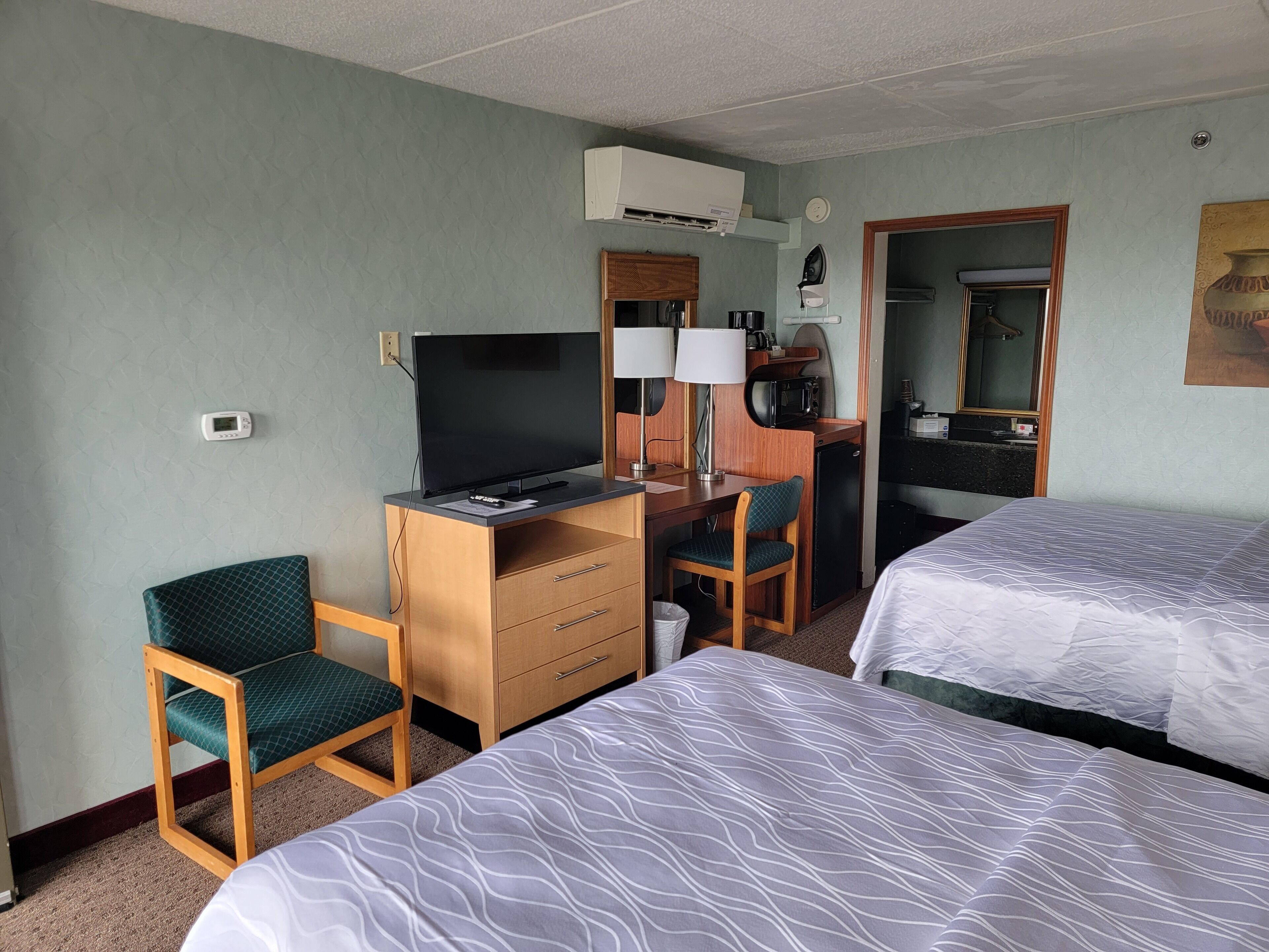 Ein Hotelzimmer mit zwei Betten, einem Schreibtisch mit Computer, einem Sessel, einer Kaffeemaschine und einer Klimaanlage.