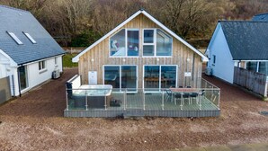 Ein modernes Holzhaus mit Glasbalkon, Whirlpool und Blick auf eine bewaldete Landschaft.