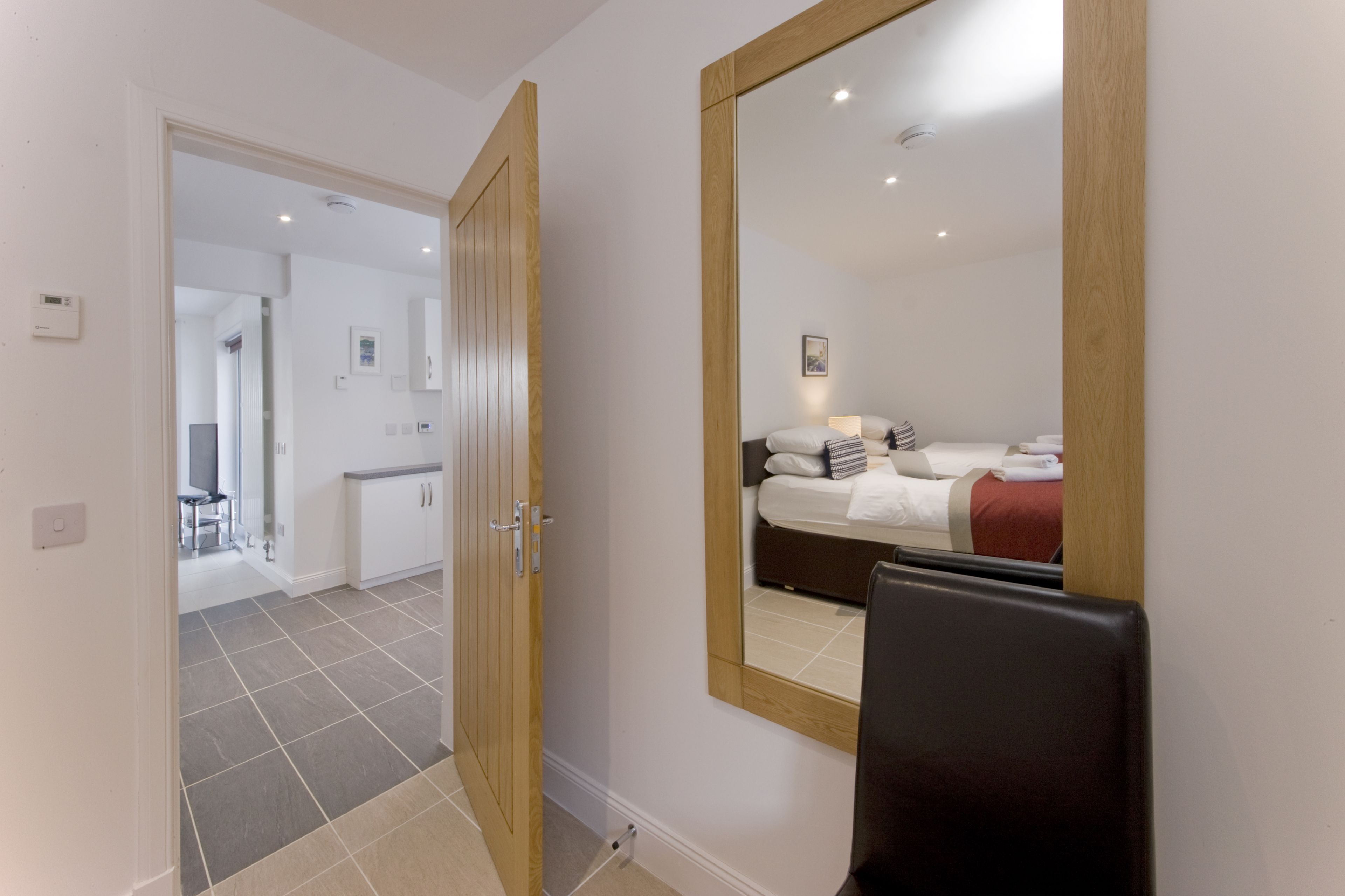 A hotel room with a large mirror, a bed with white linens, a bedside table, and a chair.