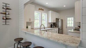 Una cocina moderna con armarios blancos, encimera de mármol y una estantería para vinos.