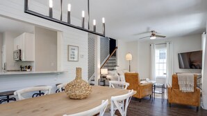 Un comedor moderno con una mesa de madera y sillas blancas, una escalera con barandilla decorativa y un ventilador de techo.
