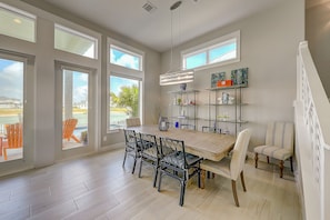 A dining area with a wooden table, black chairs, and a chandelier. There are large windows with views of the outdoors.