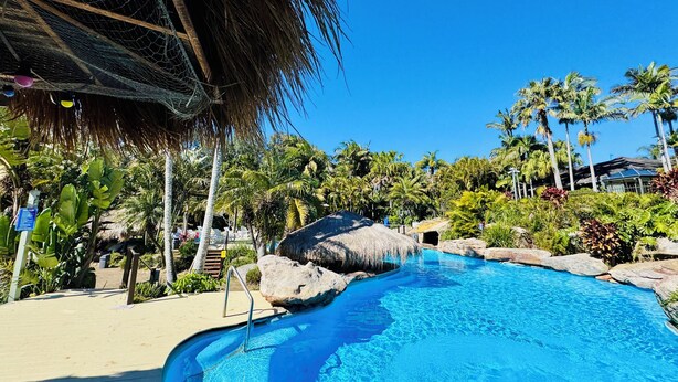 A clear blue pool with a thatched roof structure, surrounded by palm trees and rocks. - Reef @ Aanuka Beach Resort Pool / Spa / Tennis (Coffs Harbour)