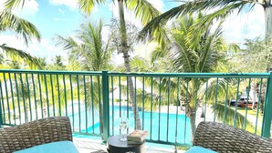 A balcony with wicker furniture, a pool, and palm trees. - Luxurious Waterfront Stay w/ Large Sun Deck (Providenciales)