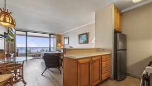 A modern kitchen with wooden cabinets, a stainless steel refrigerator, and a dining area with wicker chairs. - Direct Oceanfront Studio with 180 Degrees Ocean View in Maui Kaanapali Beach (Lahaina)