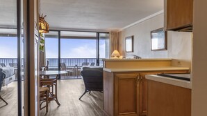 A hotel room with a balcony, a dining area with chairs, a kitchen with wooden cabinets, and a view of the sea. - Direct Oceanfront Studio with 180 Degrees Ocean View in Maui Kaanapali Beach (Lahaina)