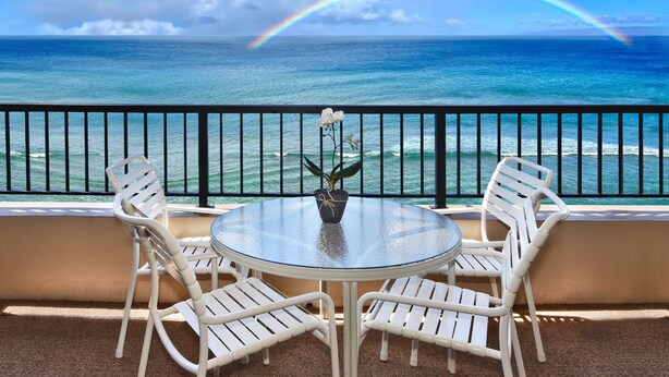 A balcony with a glass table and white chairs, overlooking the ocean with a rainbow. - Direct Oceanfront Studio with 180 Degrees Ocean View in Maui Kaanapali Beach (Lahaina)