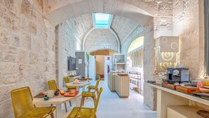 A narrow, stone-walled corridor leading to a dining area with yellow chairs and tables, a kitchen area with a coffee machine, and a TV mounted on the wall. - Bed & Breakfast in Ostuni with 1 bedrooms sleeps 2 (Ostuni)