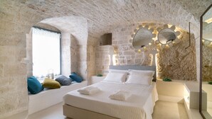 Ein Schlafzimmer mit einer Steinswand, einem großen Bett mit weißer Bettwäsche und einem Spiegel mit dekorativer Beleuchtung.