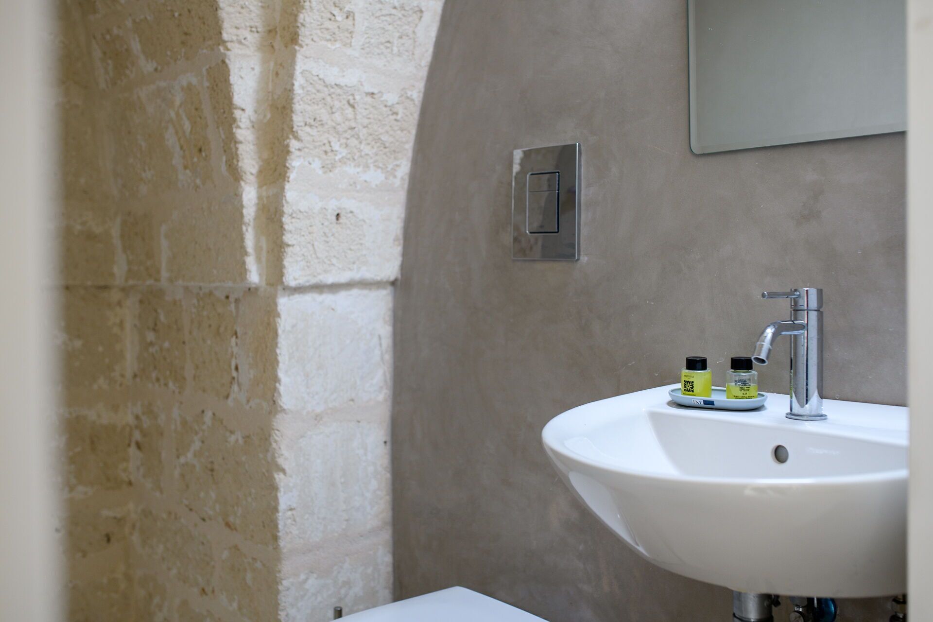 A bathroom with a white sink, a mirror above it, and a small shelf with toiletries.