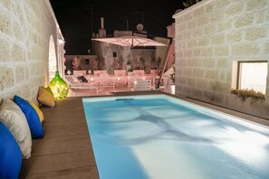 Relax by the pool surrounded by a low wall and lounge chairs under a shaded area.