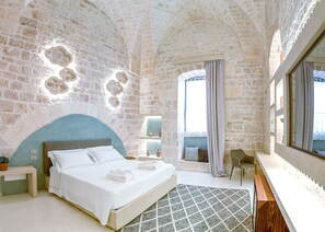 Experience the unique charm of this hotel room, featuring a vaulted ceiling and a stone wall, with a comfortable bed and stylish seating area.