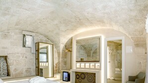 A modern bedroom with a stone wall, a large bed, a mirror, a TV, and a shower area. - Bed & Breakfast in Ostuni with 1 bedrooms sleeps 2 (Ostuni)