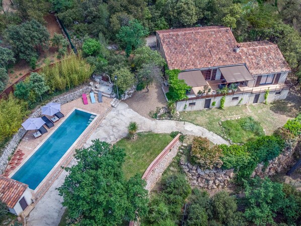 Vue aérienne d’une propriété dotée d’une piscine, d’un espace salon extérieur et d’une grande maison avec un toit en tuiles.