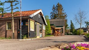 Un bâtiment à la façade en briques, doté d’un toit en tuiles et d’un petit espace extérieur aménagé avec des sièges et un chariot en bois.