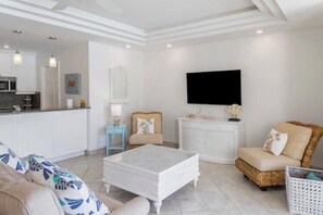 A modern living room with a white coffee table, a sofa, a wicker chair, and a television mounted on the wall. - Romantic Escape with Stunning Pools & Sunset Views (Providenciales)