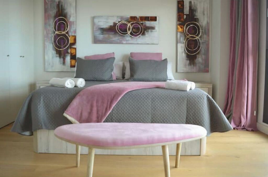 Een slaapkamer met een bed, kussens, een bankje en kunst aan de muur.