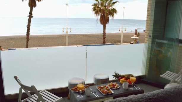 A balcony with a table set for breakfast, overlooking a beach with palm trees and the ocean. - MALAGA BEACHFRONT PARADISE (Malaga)