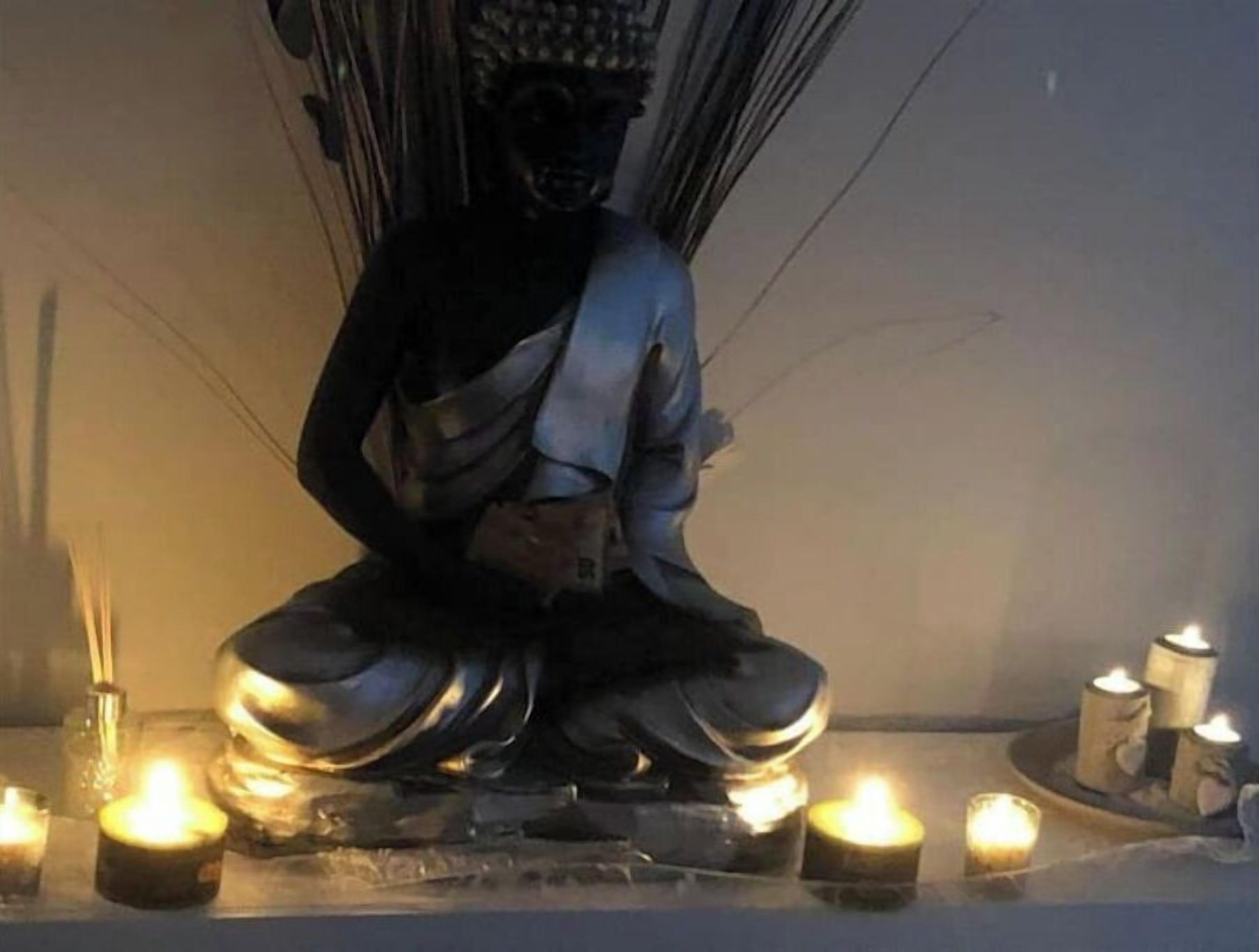A statue of a seated figure with a draped robe, surrounded by lit candles on a reflective surface.