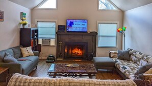Ein gemütliches Wohnzimmer mit Kamin, zwei Sofas, einem Couchtisch und einem Fernseher, der "WELCOME" anzeigt.