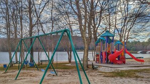 Ein Spielplatz mit Schaukeln und Rutsche, umgeben von Bäumen und einem See.
