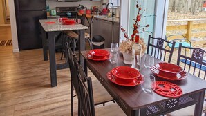 Eine moderne Küche mit grauen Schränken, einem schwarzen Kühlschrank und einer Mikrowelle. Ein Esstisch mit roten Tellern und Gläsern, und eine Vase mit Blumen.