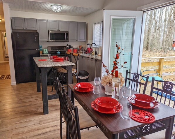A modern kitchen with grey cabinets, a black refrigerator, and a microwave. There is a dining table with red plates and glasses, and a vase with flowers.