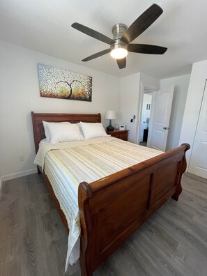 Une chambre avec un lit en bois, un ventilateur de plafond et un tableau accroché au mur.