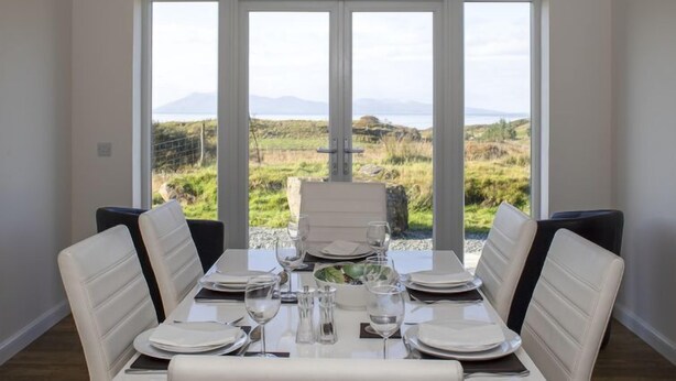 A dining area with a table set for four, large windows offering a view of a grassy landscape and mountains.