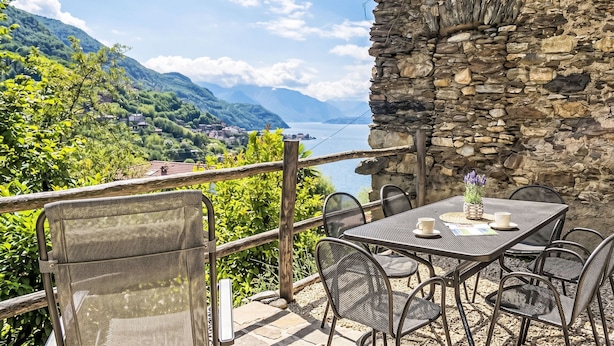 A terrace with outdoor seating, a stone wall, and a scenic view of mountains and a lake.