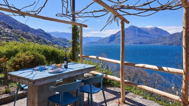 Ein Essbereich im Freien mit Tisch und Stühlen, mit Blick auf einen See und Berge.