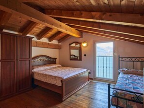 A bedroom with a wooden ceiling, a bed, a wardrobe, and a balcony with a view.
