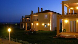 A modern two-story house with a balcony, a well-lit entrance, and a visible chimney. - Antonios Village (Pineios)