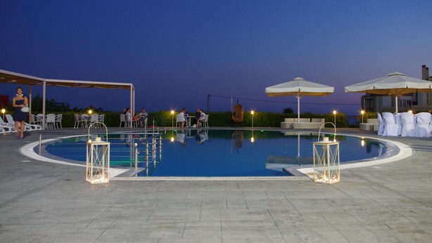 A swimming pool with lounge chairs and umbrellas, surrounded by a covered seating area. - Antonios Village (Pineios)