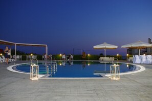 Una piscina con sillas de descanso y sombrillas, rodeada de un área de estar techada.