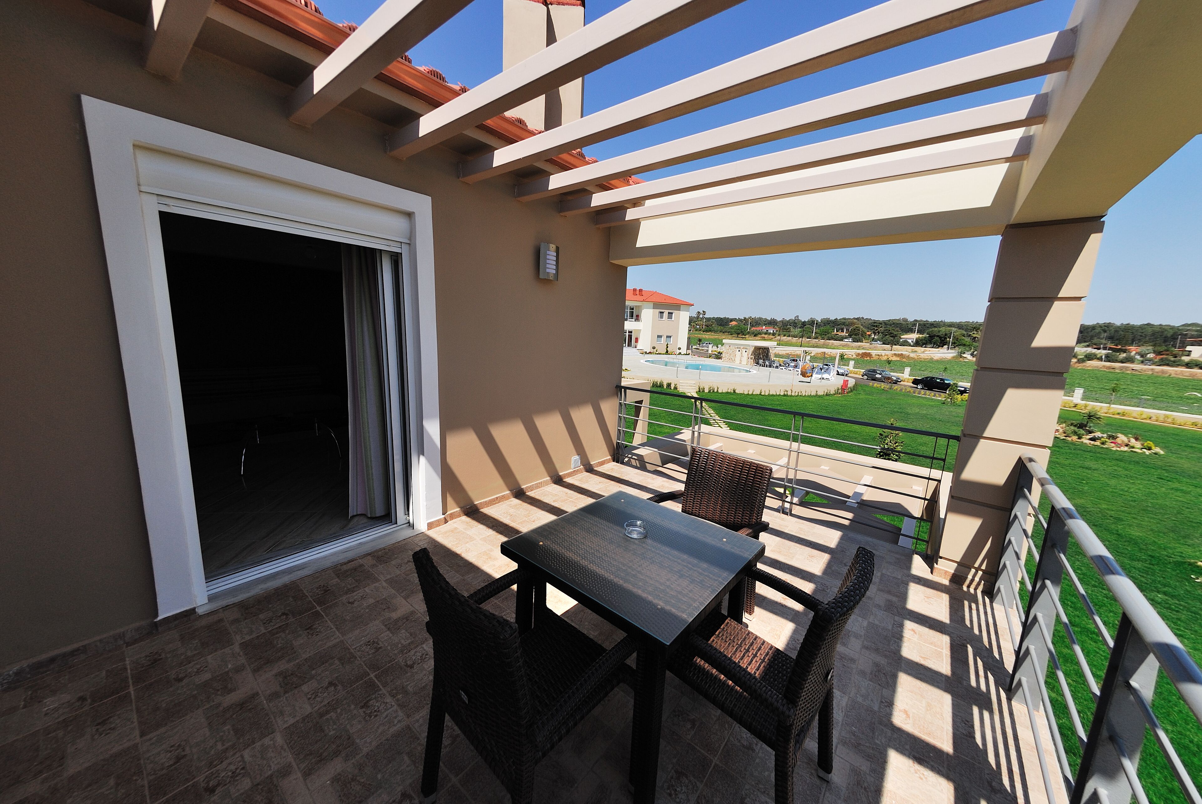 A balcony with a table and chairs, a view of a swimming pool, and a grassy area in the background.