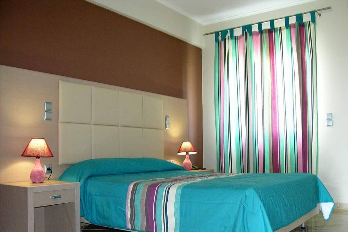 A bedroom with a bed, two bedside lamps, a nightstand, and a striped curtain.